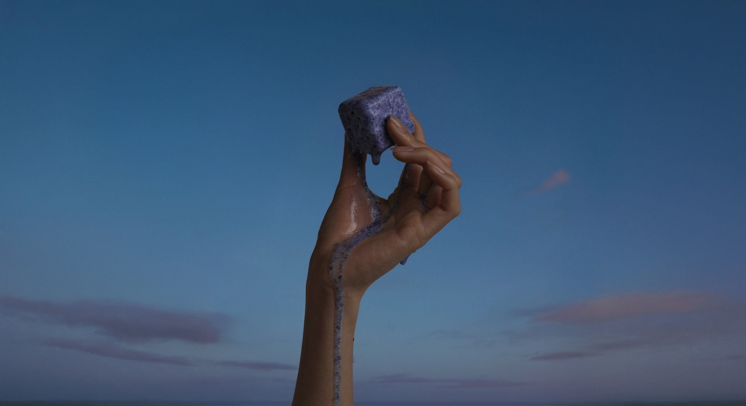 Hand holding a Shower Story shower steamer against a dusk sky with clouds